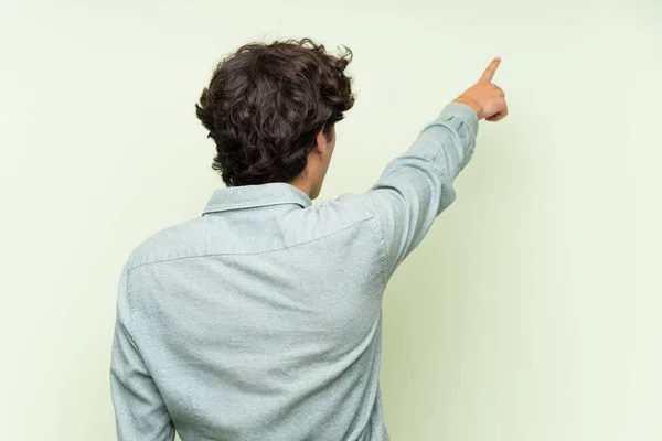 Joven Sobre Pared Verde Aislada Apuntando Hacia Atrás Con Dedo —  Fotos de Stock