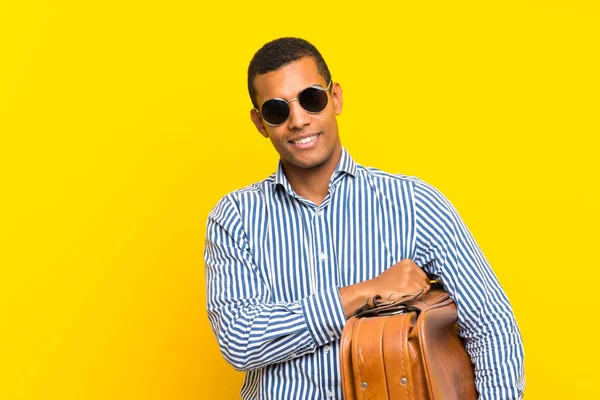 Hombre morena sosteniendo un maletín vintage sobre fondo amarillo aislado —  Fotos de Stock