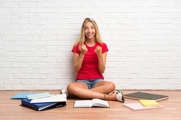 Young Blonde Student Girl Many Books Floor Celebrating Victory — Stock Photo, Image