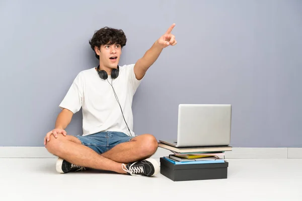 ノートパソコンを持った若い男が床を指差して座っている — ストック写真