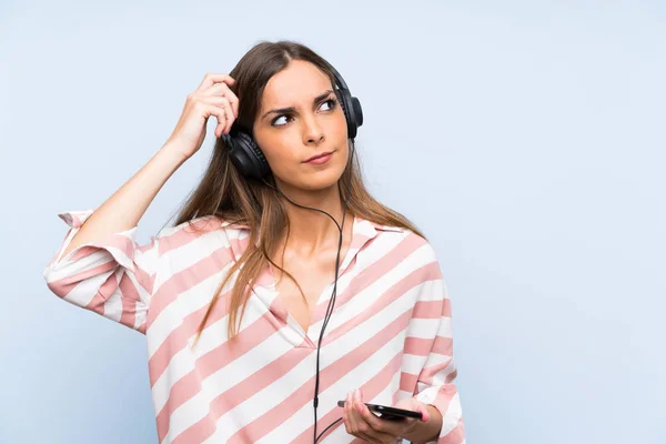 Mujer Joven Escuchando Música Con Móvil Sobre Una Pared Azul —  Fotos de Stock