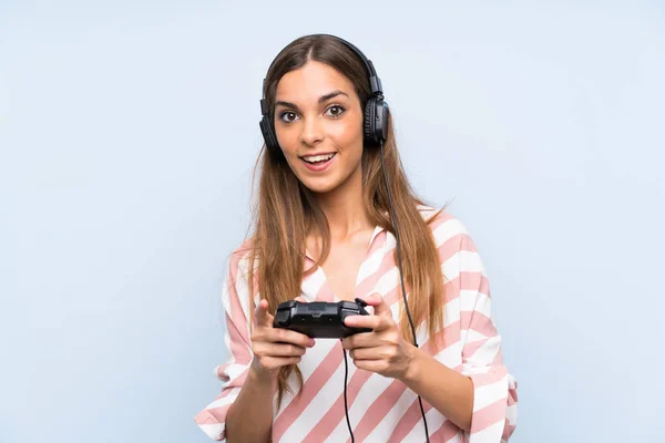 Mujer joven jugando con un controlador de videojuegos sobre una pared azul aislada —  Fotos de Stock