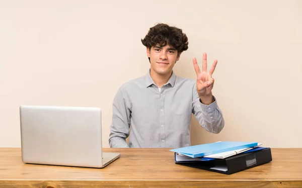 Young student man with a laptop happy and counting three with fingers