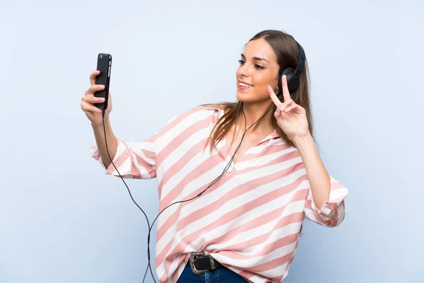Mladá žena naslouchající hudbě s mobilním přes izolované modré Wal — Stock fotografie