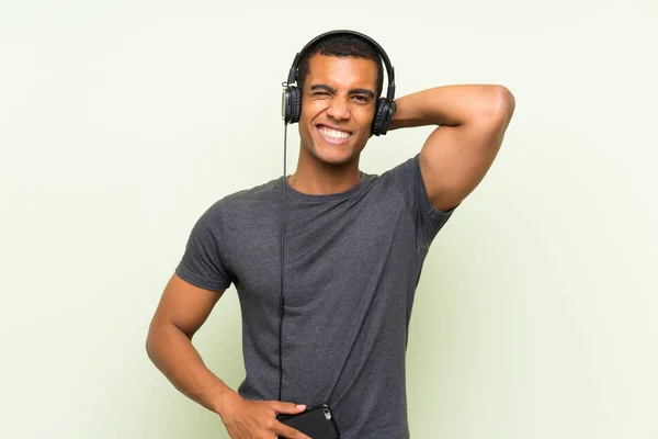 Junger gutaussehender Mann hört Musik mit Handy über isolierte grüne Mauer — Stockfoto