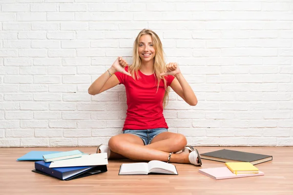 Young blonde student girl with many books on the floor proud and self-satisfied