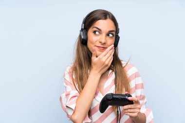 Genç kadın izole mavi duvar üzerinde bir fikir düşünme üzerinde bir video oyunu denetleyicisi ile oynuyor