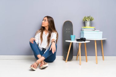 Genç bir kadın yerde oturuyor, yan tarafa bakıyor.