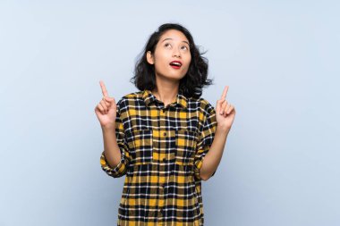 Izole mavi arka plan üzerinde Asyalı genç kadın şaşırttı ve işaret