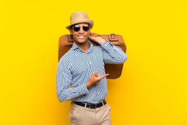 Esmer adam izole sarı arka plan üzerinde bir vintage evrak çantası tutan şaşırttı ve yan parmak işaret