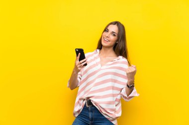 Zafer pozisyonunda telefon ile izole sarı arka plan üzerinde genç kadın