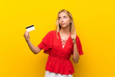 Bir kredi kartı tutan izole sarı arka plan üzerinde Sarışın genç kadın