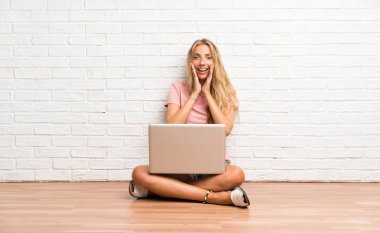 Sürpriz yüz ifadesi ile katta bir dizüstü bilgisayar ile genç sarışın öğrenci kız