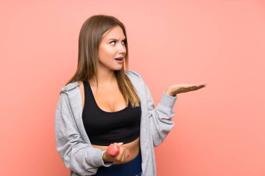 Genç spor kız sürpriz yüz ifadesi ile izole pembe arka plan üzerinde halter yapma