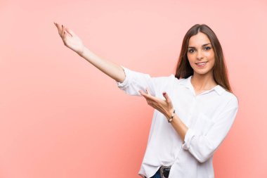 Soyutlanmış pembe arka planda genç bir kadın. Davet edilmek için ellerini yana uzatıyor.