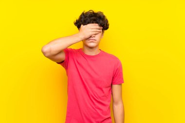 Gözleri elleriyle kaplayan izole sarı duvarın üzerindeki genç adam