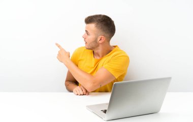 İşaret parmağı yla geri işaret eden bir dizüstü bilgisayar ile bir masada genç sarışın adam