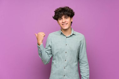 Izole mor duvar üzerinde genç adam bir ürün sunmak için yan işaret