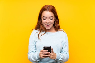 Izole sarı arka plan üzerinde genç redhead kız cep ile bir mesaj gönderme