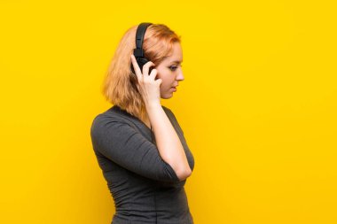 Izole sarı arka plan üzerinde genç kadın kulaklık ile müzik dinlerken