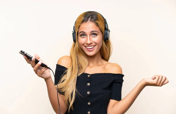 Молодая блондинка слушает музыку с мобильного на изолированном фоне — стоковое фото
