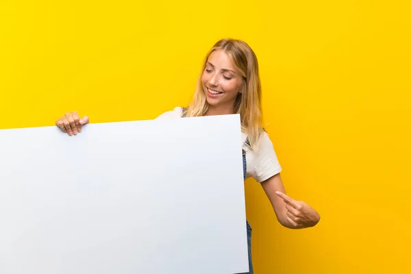 金发年轻女子在孤立的黄色背景拿着一个空的白色标语牌插入一个概念 — 图库照片