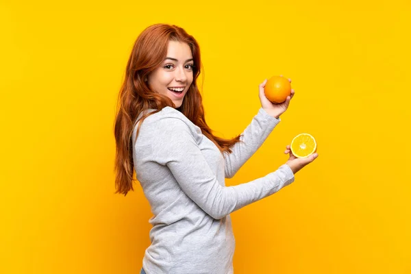 Genç kızıl saçlı kız izole sarı arka plan üzerinde bir portakal tutan — Stok fotoğraf