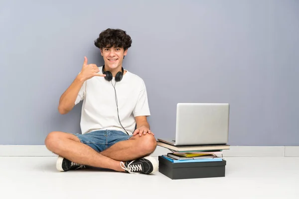 彼のラップトップを持つ若い男は 1つの床に座って電話ジェスチャーを作ります — ストック写真