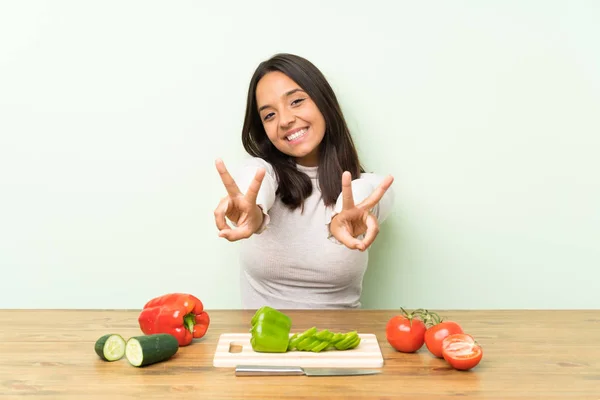 Young brunette woman with vegetables smiling and showing victory sign