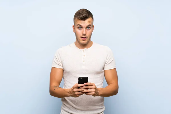 Joven Guapo Hombre Rubio Sobre Fondo Azul Aislado Usando Teléfono —  Fotos de Stock