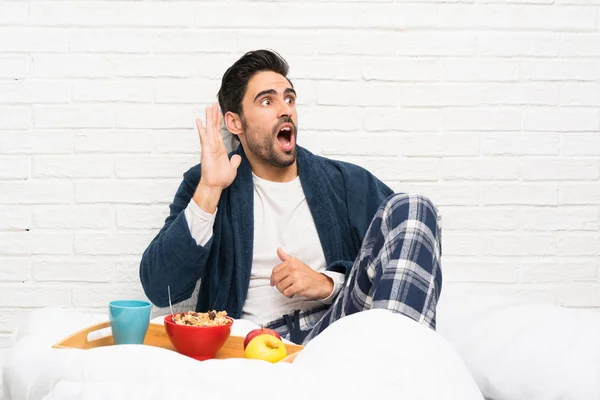 Man in bed with dressing gown and having breakfast shouting with mouth wide open