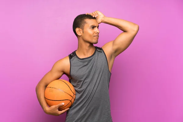 Young sport man with ball of basketball over isolated purple wall having doubts and with confuse face expression