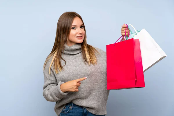 ショッピングバッグの多くを保持する孤立した青い背景の上にセーターを持つティーンエイジャーの女の子 — ストック写真