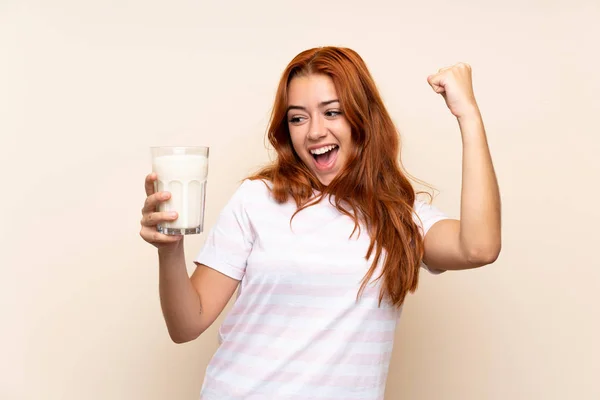 青少年红发女孩拿着一杯牛奶在孤立的背景庆祝胜利 — 图库照片