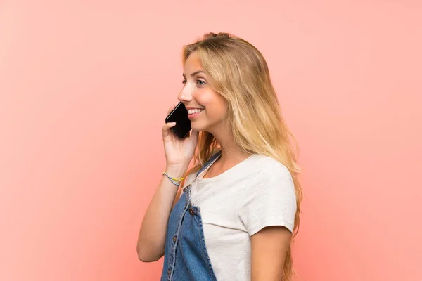 Mujer joven rubia feliz con un teléfono móvil sobre una pared rosa aislada — Foto de Stock