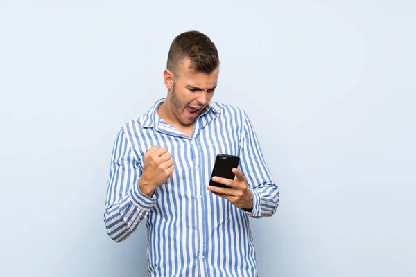 Joven Guapo Hombre Rubio Sobre Fondo Azul Aislado Con Teléfono — Foto de Stock