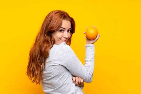 십대 빨간 머리 소녀 들고 오렌지 위에 고립 된 노란색 배경 — 스톡 사진