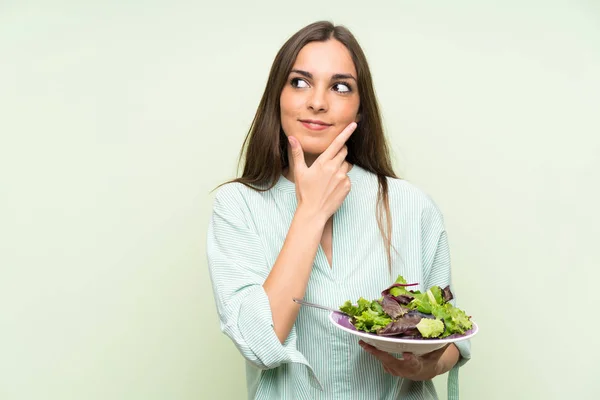 Mujer Joven Con Ensalada Sobre Una Pared Verde Aislada Pensando — Foto de Stock