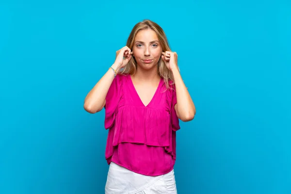 Bionda Giovane Donna Isolato Sfondo Blu Frustrato Coprendo Orecchie — Foto Stock