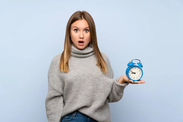 Adolescente Menina Com Suéter Sobre Isolado Fundo Azul Segurando Relógio — Fotografia de Stock