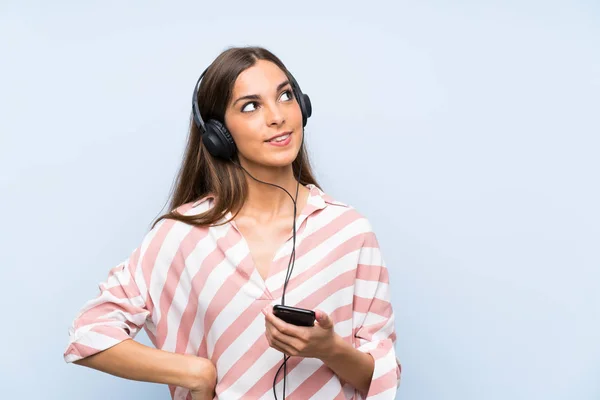 Jonge Vrouw Luisteren Muziek Met Een Mobiele Geïsoleerde Blauwe Muur — Stockfoto