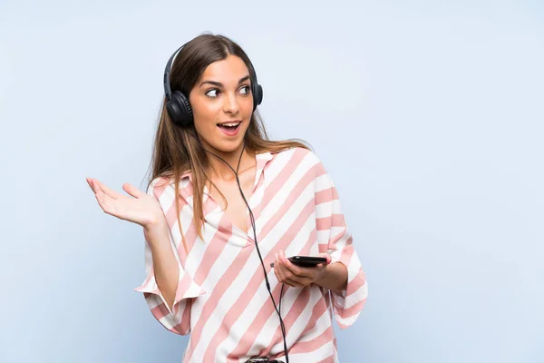 Mujer Joven Escuchando Música Con Móvil Sobre Una Pared Azul —  Fotos de Stock