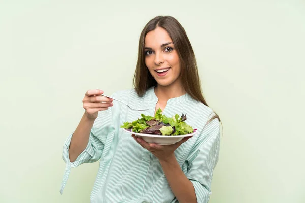 Jonge vrouw met salade over geïsoleerde groene muur — Stockfoto