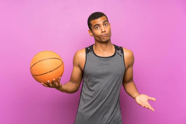 Young sport man with ball of basketball over isolated purple wall making doubts gesture while lifting the shoulders