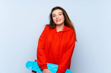 Genç esmer kız izole edilmiş mavi arka planda kaykay yapıyor.