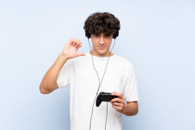 Genç adam izole mavi duvar gururlu ve kendinden memnun üzerinde bir video oyunu denetleyicisi ile oynuyor