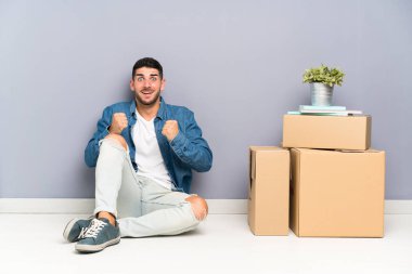 Yakışıklı genç adam bir zafer kutluyor kutuları arasında yeni bir evde hareket