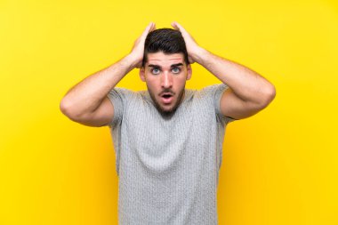 Sürpriz yüz ifadesi ile izole sarı arka plan üzerinde genç yakışıklı adam