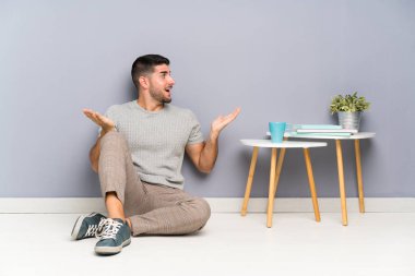 Genç yakışıklı bir adam yerde oturuyor ve yüzünde sürpriz bir ifade var.