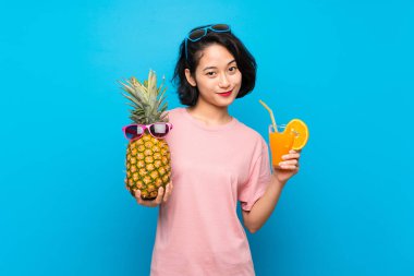 Güneş gözlüğü ile bir ananas tutan izole mavi arka plan üzerinde Asya genç kadın
